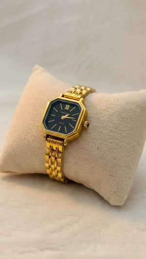 Gold watch with a black face on a beige cushion