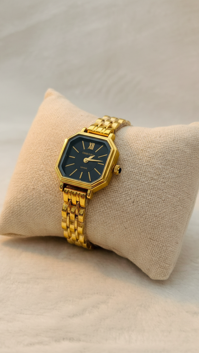 Gold watch with a black face on a beige cushion